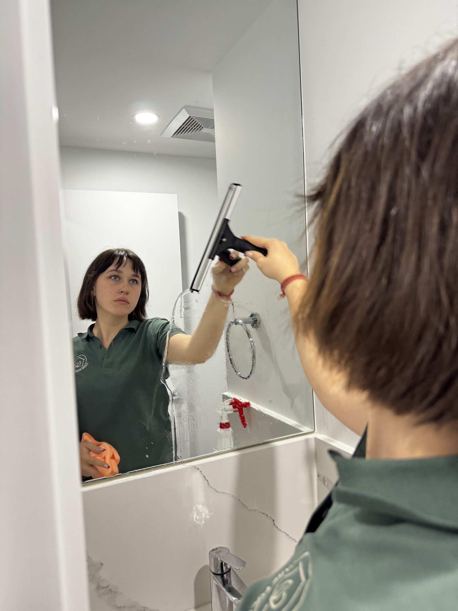 A Care for a Clean team member cleaning a bathroom mirror streak-free