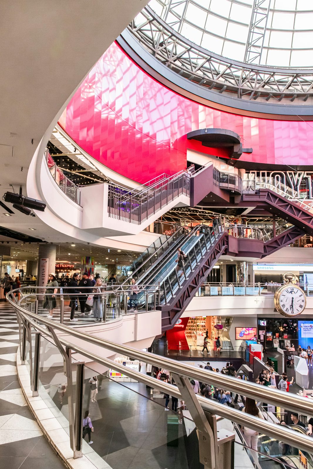 A busy shopping centre atrium with escalators and walkways kept clean through trading hours